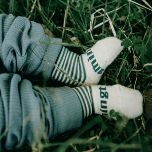 Merino Wool Crew Socks for Baby in Tui with oatmeal and green stripes, resting on grass.