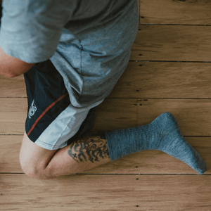 Man wearing Merino Wool Crew Socks in grey while kneeling on wooden floor.