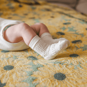 Merino Wool Crew Socks | BABY | Pearl on a baby lying on a yellow floral blanket, showcasing zigzag texture and softness.