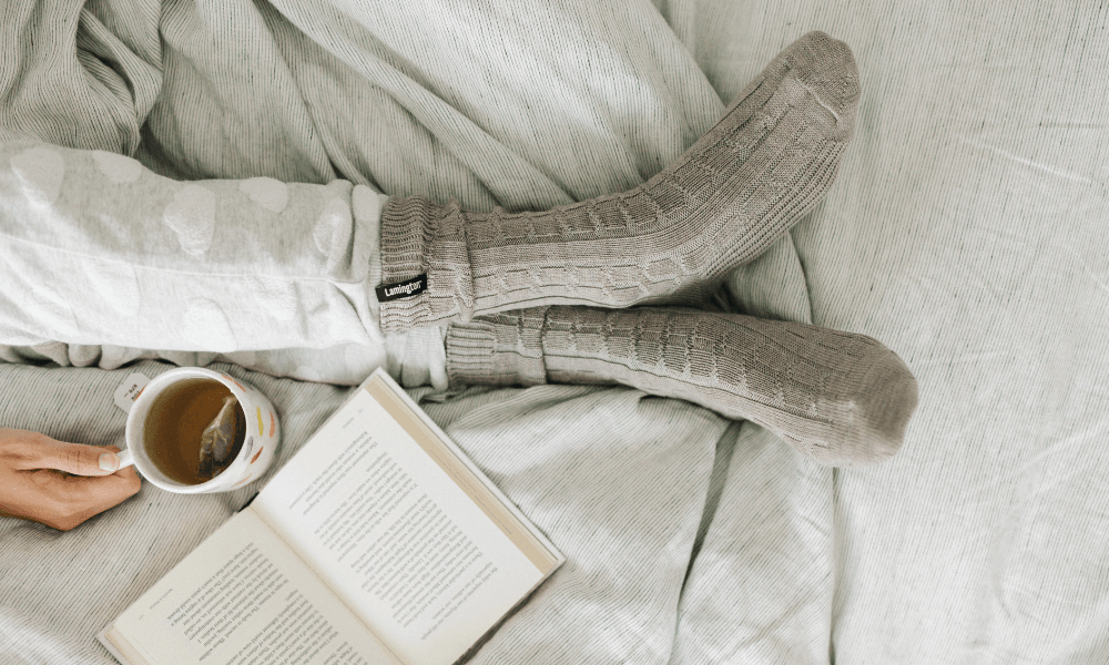 Cosy feet in grey socks while reading a book and sipping tea
