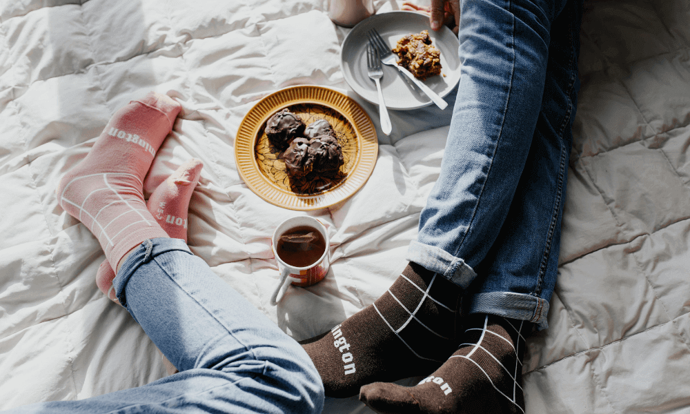 feet in merino socks for everyday wear enjoying snacks and coffee on a bed.