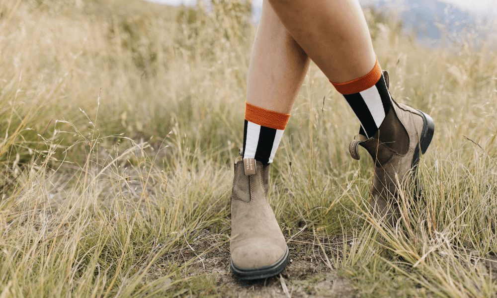 A close-up of legs in stylish boots and colorful socks in a grassy outdoor setting, perfect travel companions for adventures.