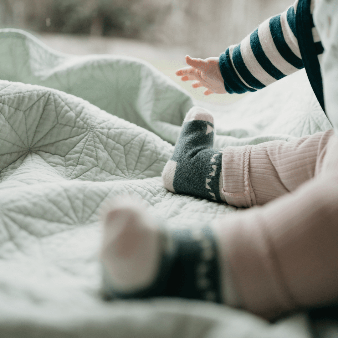 Baby wearing Merino Wool Baby Socks, reaching out on a soft quilted blanket.