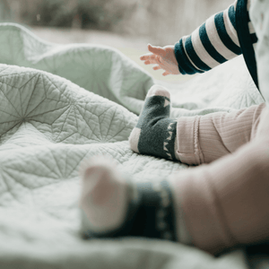 Baby wearing Merino Wool Baby Socks, reaching out on a soft quilted blanket.