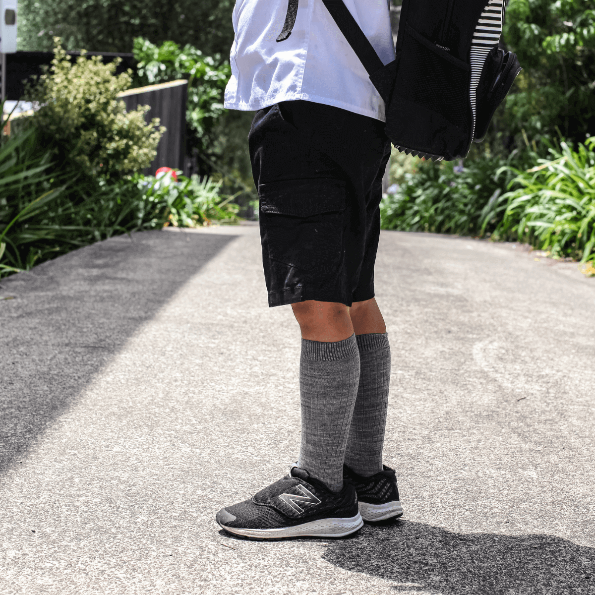 Merino Wool Knee High Socks for children worn with black shorts and sneakers in a park setting.