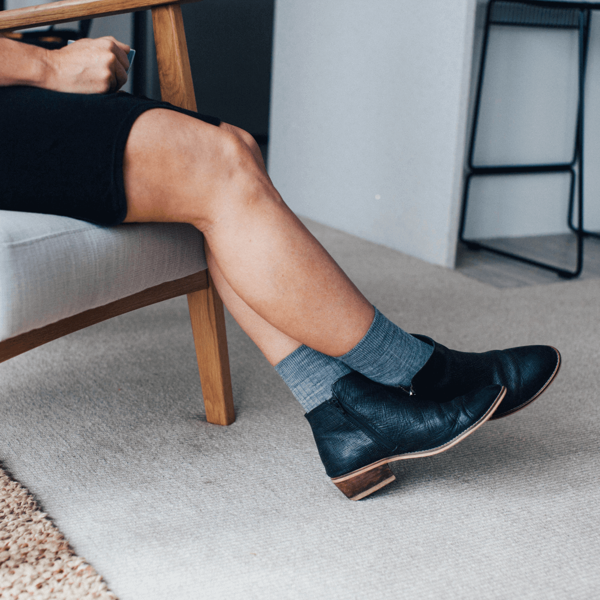 Woman wearing Merino Wool Crew Socks in Grey with black ankle boots, sitting on a chair.
